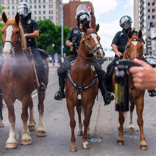 A law enforcement official ejects pepper spray from a canister with police on horses in the background at a George Floyd protest in Columbus, Ohio.